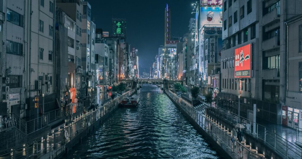 導入文 日本には多様な方言が存在しますが、その中でも特に人々を惹きつけるのが関西弁です。独特のイントネーションや豊かな表現力、そしてお笑い文化と深く結びついたユーモラスな言葉遣いは、全国的に親しまれています。本記事では、そんな関西弁の中でも近年注目を集める「生きとったんかワレ」という表現に焦点を当て、その意味や使われ方、文化的な背景について詳しく解説していきます。 関西弁の魅力とは？ 関西弁とは何か？その特色を知ろう 関西弁は、大阪や京都、兵庫、奈良、滋賀、和歌山など関西地方一帯で広く使われる方言で、親しみやすくユーモラスな響きを持っています。標準語と比べてもイントネーションの抑揚が大きく、独特のリズムやアクセントが特徴的です。例えば「ほんま」「せやな」「ちゃうねん」といった言い回しは、相手に柔らかく、時には力強くメッセージを伝える役割を果たします。こうした独自性から全国的にも人気が高く、テレビやラジオ、さらにお笑い文化を通じて広く浸透し、関西弁を耳にするだけで明るく楽しい雰囲気をイメージする人も少なくありません。さらに、最近ではSNSや動画配信を通じて若い世代にも支持を集め、日常会話にちょっとしたスパイスを加える表現として親しまれています。 関西弁の歴史と文化的背景 関西弁は古くから京都を中心に発展してきました。京都は長らく都であったため、公家や武家の言葉遣いに影響を受けつつも、庶民の生活に根付いた独自の表現が育まれていきました。特に大阪は商人の町として発展し、取引や交渉の場面で機知に富んだやり取りが重視されました。その結果、洒落や皮肉を込めた表現が数多く生まれ、現代の「ボケとツッコミ」の文化にもつながっています。また、落語や漫才といった伝統芸能を通して関西弁は全国に広まり、親しみやすく、時に鋭い言葉遣いとして定着しました。今日でもテレビ番組や舞台芸能では欠かせない要素となっており、関西弁そのものがエンターテインメントの一部と見なされています。 関西弁のコミュニケーション能力について 関西弁は、相手との距離を縮める効果が非常に高いと言われています。日常会話では自然に笑いやツッコミが入りやすく、会話がリズミカルに展開されるため、相手との心理的距離を一気に縮めることができます。例えば初対面の相手でも「どないやねん」「なんでやねん」といったフレーズを交えることで、場の空気が柔らかくなり、堅苦しさを和らげます。また、ユーモアを交えたやり取りが相手に安心感を与え、親しみやすい雰囲気を作り出すため、コミュニケーションを円滑にする強力な武器となります。さらに、感情表現の幅が広いため、怒りや喜び、驚きなどをより生き生きと伝えられるのも大きな魅力です。 「生きとったんかワレ」の意味 「生きとったんかワレ」の語源と成り立ち 「生きとったんかワレ」は直訳すると「まだ生きていたのか、お前」という意味になります。関西弁特有の砕けた言い回しで、驚きや懐かしさを強調する表現です。元来は親しい間柄での軽い冗談として使われ、再会の喜びをコミカルに伝える言葉でした。近年はネット掲示板「なんJ」などで頻繁に使われ、ネットスラングとして広まった背景があります。さらにYouTubeやSNSでの配信文化が拡大したことで、若い世代の間でもミーム的に用いられるようになり、関西弁を知らない人にまで定着しています。語源的には「生きていたのか」と「ワレ（お前）」を組み合わせたシンプルな構造ですが、イントネーションや言い方によってニュアンスが大きく変化する点が特徴です。 使われるシチュエーションを深掘り 主に久しぶりに再会した相手に対して冗談めかして使われます。例えば長期間連絡がなかった友人に出会った時、「お前、まだ生きとったんかワレ！」と声をかけることで、再会の喜びや親しさをユーモラスに表現します。時には飲み会や同窓会の席で、笑いを誘う一言として飛び出すこともあります。真剣に言うのではなく、あくまで軽妙なトーンで使うのがポイントで、相手との関係性が近しいほど効果的に働きます。また、SNSやチャット上でも「久々の投稿」に対してコメントする形で用いられることがあり、文字だけでも親しさを演出できる便利なフレーズです。 対話における「生きとったんかワレ」の役割 このフレーズは、相手を笑わせたり、会話を盛り上げたりする役割を担います。単なる驚きの言葉ではなく、相手を大切に思う気持ちや再会の喜びをユーモアに包んで伝えるための表現です。相手を否定するのではなく、むしろ関係性の深さを表すユーモアとして用いられます。親しみの証としての冗談であり、気心の知れた関係だからこそ成立するやり取りです。 「生きとったんかワレ」の具体例 人気のスタンプや素材をチェック LINEスタンプやSNSの素材として「生きとったんかワレ」は人気を集めています。コミカルなイラストと組み合わされることで、気軽に使えるジョーク表現として親しまれています。特にLINEスタンプでは、関西弁特有のイントネーションを文字と表情豊かなキャラクターで表現することで、メッセージのやり取りがさらに楽しくなると好評です。SNSでは画像やGIFアニメとともに投稿されることも多く、見る人の笑いを誘う定番ネタの一つになっています。TwitterやInstagramでも「#生きとったんかワレ」といったハッシュタグが使われ、ユーザー同士のちょっとした冗談や再会の報告に添えられるケースが増えています。 「生きとったんかワレ」を用いた漫画の紹介 関西弁キャラクターが登場する漫画やギャグ作品では、このフレーズが効果的に用いられることがあります。キャラクター同士の掛け合いを強調するための決まり文句としても定番です。特にギャグ漫画では、久々に登場したキャラクターへのツッコミとして読者の笑いを誘う役割を果たしています。また、同人誌や二次創作の世界でもネタ的に使用されることが多く、関西弁の雰囲気を盛り上げるアイテムの一つとなっています。こうした描写は、読者にキャラクター同士の距離感や親しみを直感的に伝える効果があります。 なんJでの使用例を学ぶ ネット掲示板「なんJ」では、スレッドに久々に現れたユーザーや意外な話題に対して「生きとったんかワレ！」と書き込むのが定番。ネット文化の中で愛される表現となっています。さらに、スレッドが過去の話題を蒸し返した際にも、このフレーズで茶化すことで場を和ませることがあります。短いながらもユーモラスな言葉であるため、ネット上での共感や一体感を生み出す要素となり、コミュニティ文化を象徴するフレーズとして位置付けられています。 類似表現や関連表現 「生きとったんかワレ」に似た関西弁の表現 「なんや、まだおったんか」や「元気にしとったんか」なども似たニュアンスを持っています。いずれも久しぶりの再会を冗談めかして表す表現です。さらに「おお、忘れてへんかったで！」や「ほんま久しぶりやなあ」など、驚きと懐かしさを同時に伝える関西弁のフレーズも多く存在します。特に親しい友人同士では「どこ行っとったんや」「死んだんかと思ったわ」といった少し大げさな表現が好まれ、再会の場を笑いに包みます。 反応や返事で使われる他の方言 関西弁以外でも、九州弁の「おっとー、元気やったと？」のように、方言には再会を喜ぶ独自の言い回しがあります。東北弁では「おめ、まだいたのが？」、沖縄弁では「あんた、なま生きとぅたんねー」といった具合に、それぞれの地域文化に根付いた表現が存在します。これらはいずれも驚きと親しみを同時に表すニュアンスを持ち、地域ごとの人柄や気質がにじみ出ています。 方言が持つ独自の意味と文化的意義 方言は地域文化や人間関係の親密さを表す重要な要素です。「生きとったんかワレ」もまた、関西特有の人懐っこさやユーモアを映し出す表現の一つと言えます。方言を用いることで、相手との距離を一気に縮め、会話を温かみのあるものにします。加えて、世代間のつながりを示す文化的な遺産でもあり、親から子へ自然に受け継がれていく言語の財産です。現代においても方言を使うことは、自分のルーツや地域アイデンティティを誇る行為として大きな意味を持っています。 まとめ 「生きとったんかワレ」は、驚きと親しみを込めた関西弁ならではのユーモラスな表現です。もともとは親しい人との軽い冗談として使われてきましたが、近年ではネットスラングとしても広まり、多くの人が気軽に使うフレーズとなっています。その背後には、関西人特有の温かみあるコミュニケーション文化が息づいており、相手を笑わせながら距離を縮める効果が大きいのが特徴です。例えば、久々に再会した友人に使えば場が一気に和み、SNSでコメントすれば親しさを演出できます。このように方言は単なる言葉遣いにとどまらず、文化や人間関係を支える大切な要素として機能しています。方言を通して地域の文化を理解することは、単に言葉を知るだけではなく、その土地の価値観や人々の生き方を感じ取ることでもあります。結果として、より深い人間関係や会話の楽しさを味わえるだけでなく、自分自身のコミュニケーション力を豊かにするきっかけにもなるでしょう。